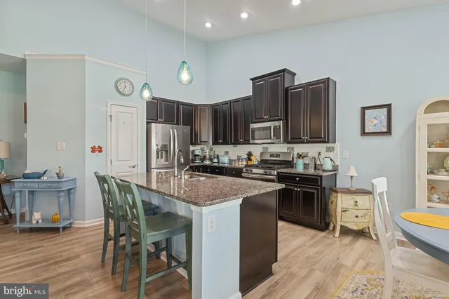 a kitchen with stainless steel appliances granite countertop a stove top oven a sink dishwasher a dining table and chairs with wooden floor