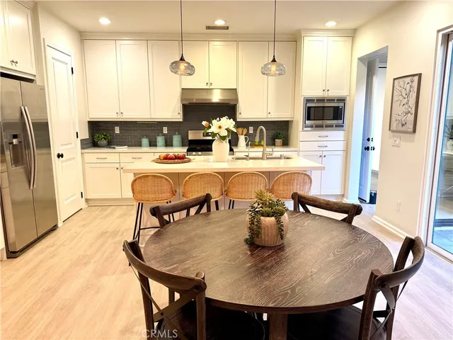 a kitchen with stainless steel appliances granite countertop a dining table chairs refrigerator and sink