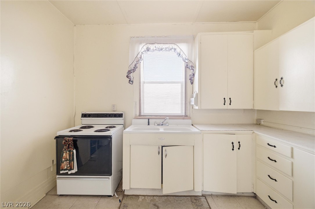 405 Main Street Beatty, NV 89003 - Photo 7 of 28 A compact kitchen with an electric range and classic white cabinetry offers functional culinary space.