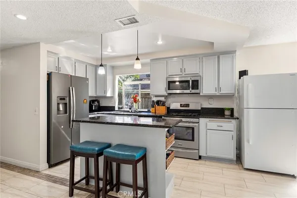 a kitchen with stainless steel appliances granite countertop a stove top oven a sink dishwasher a refrigerator and a dining table with wooden floor