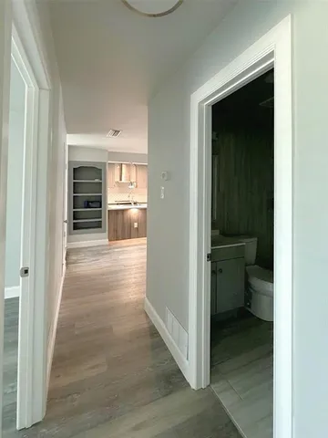 a view of a hallway with wooden floor and a bathroom