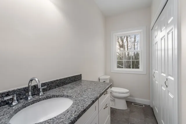 a bathroom with a granite countertop sink a toilet and a window