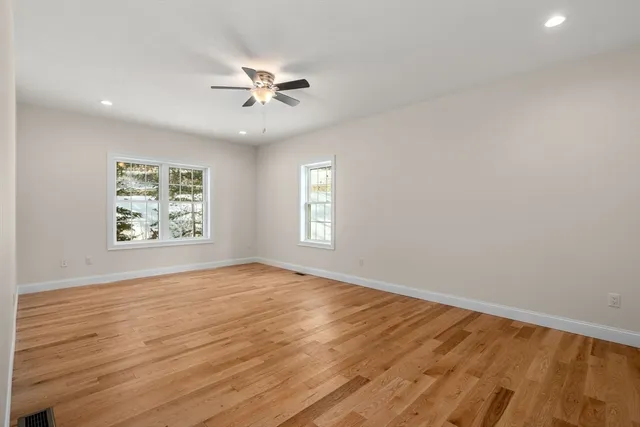 an empty room with wooden floor chandelier fan and windows