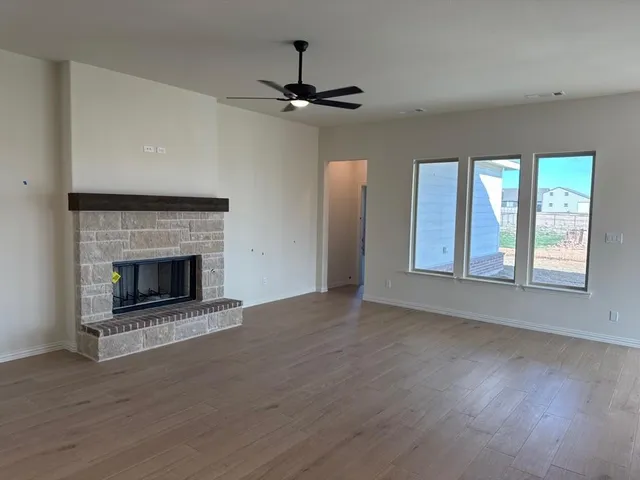 a view of an empty room with wooden floor fireplace and a window