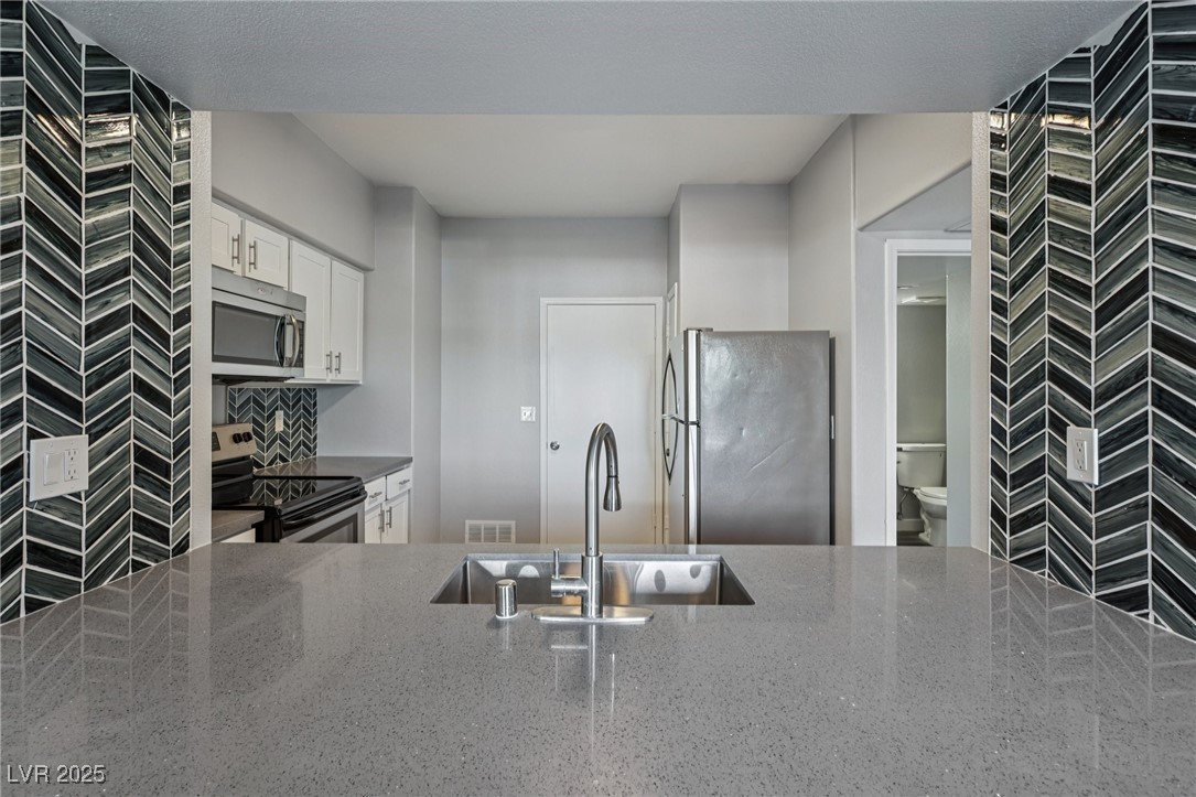 7255 West Sunset Road, Unit 1087 Las Vegas, NV 89113 - Photo 19 of 43 Kitchen with dark stone countertops, appliances with stainless steel finishes, white cabinetry, and a peninsula