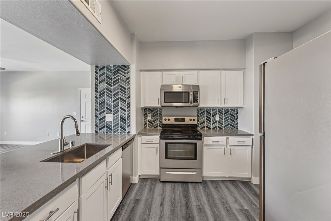 7255 West Sunset Road, Unit 1087 Las Vegas, NV 89113 - Photo 22 of 43 Kitchen featuring appliances with stainless steel finishes, backsplash, white cabinetry, dark wood-style floors, and dark stone counters