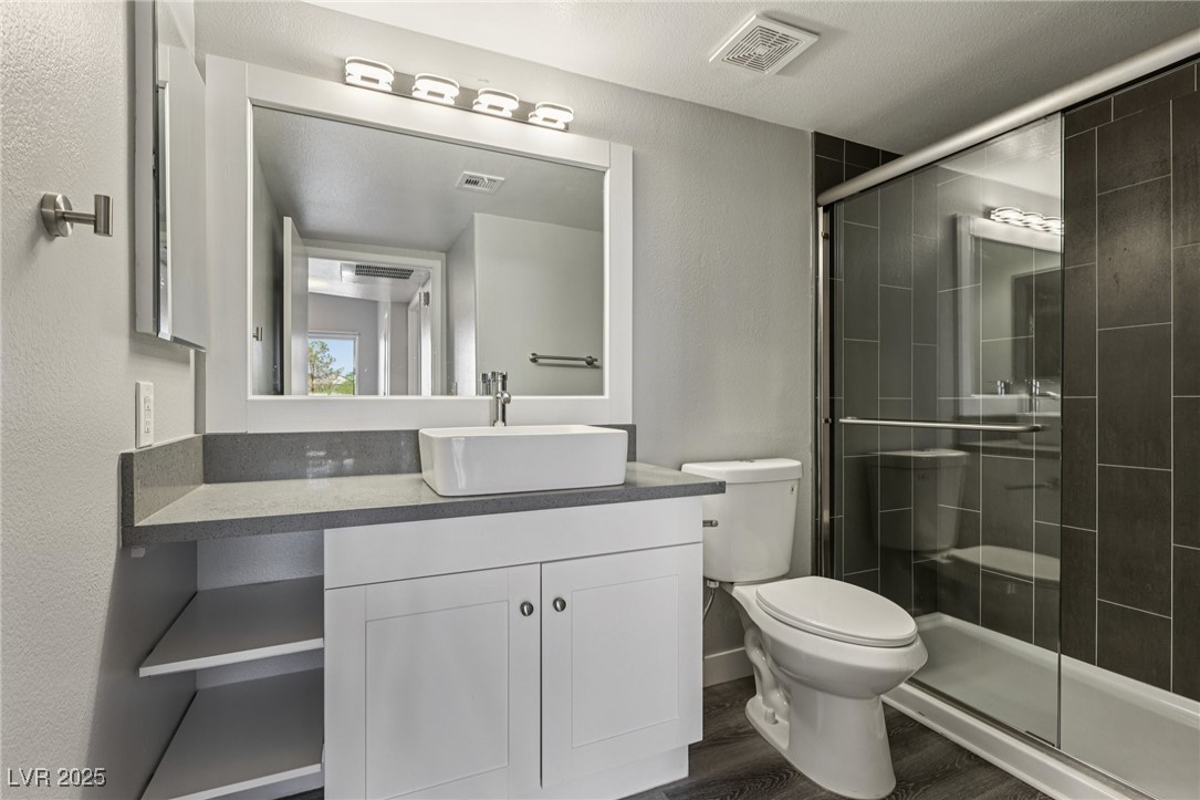 7255 West Sunset Road, Unit 1087 Las Vegas, NV 89113 - Photo 35 of 43 Full bathroom with vanity, a shower stall, dark wood-type flooring, and a textured wall