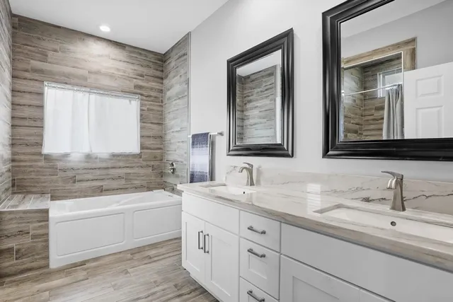 a bathroom with a double vanity sink and mirror with bathtub