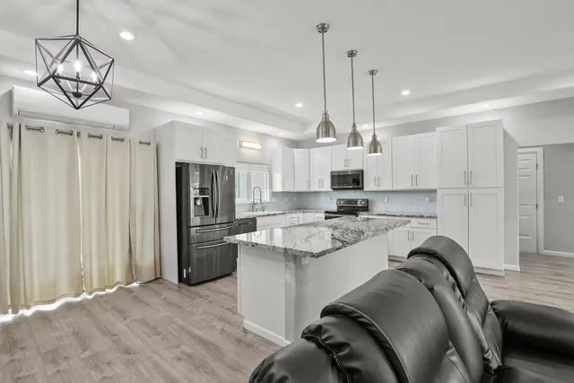 a kitchen with stainless steel appliances granite countertop a stove a sink dishwasher a refrigerator and white cabinets with wooden floor