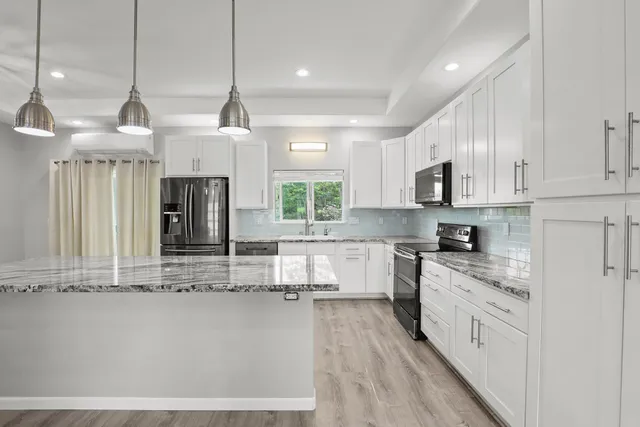 a large kitchen with stainless steel appliances granite countertop a stove a sink and white cabinets