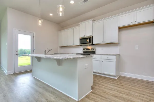 a kitchen with kitchen island granite countertop a sink a stove a microwave and wooden floors