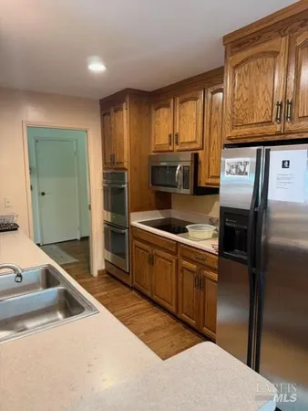 a kitchen with stainless steel appliances granite countertop a refrigerator a stove and a sink with wooden cabinets