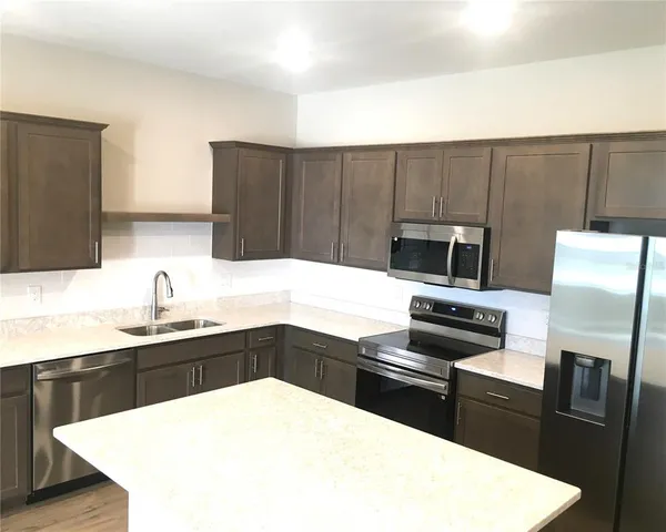 a large kitchen with a large counter top a sink stainless steel appliances and cabinets