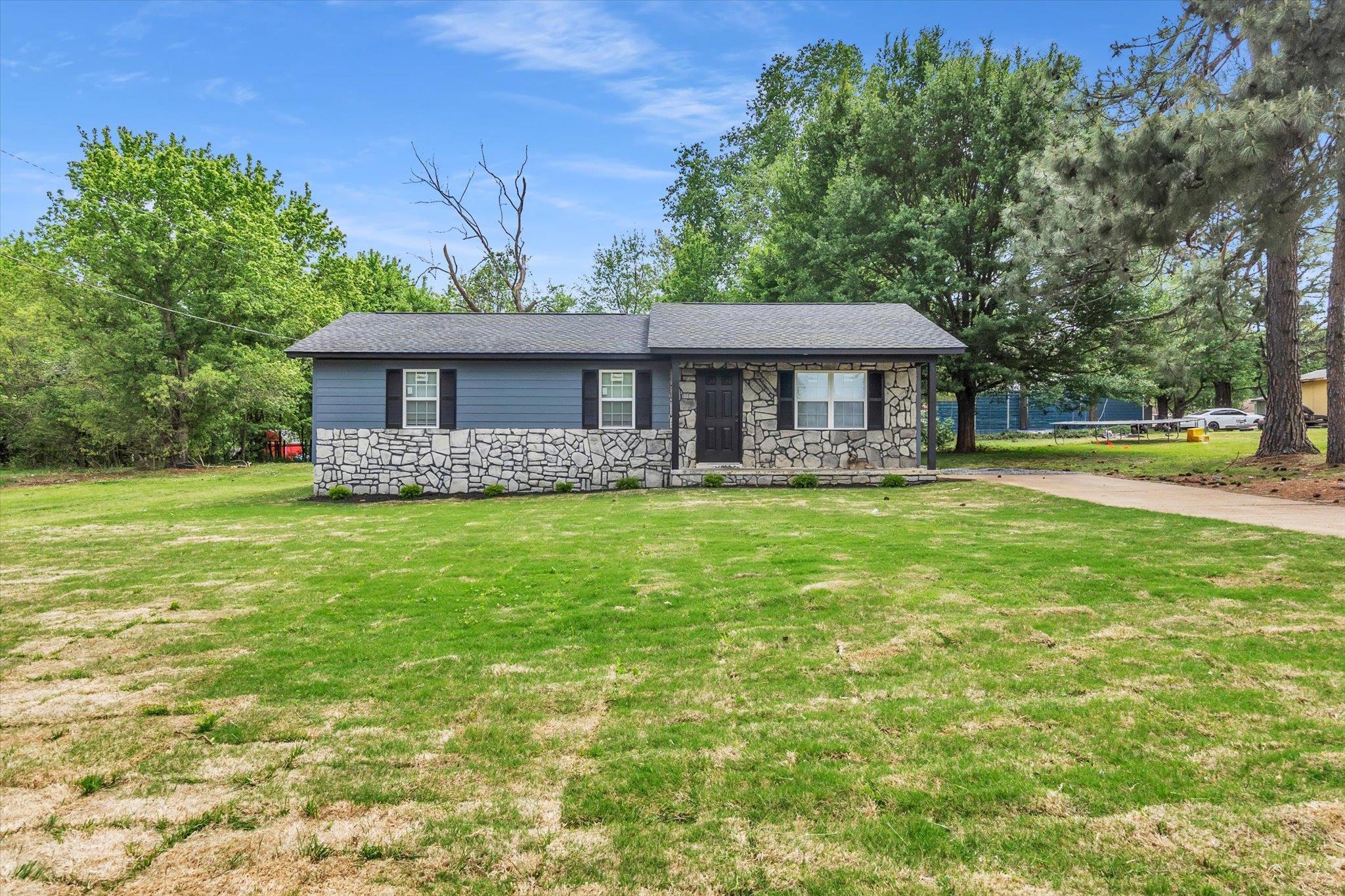 View of front of property with stone siding, a front yard, and roof with shingles
