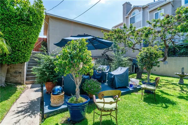 a backyard of a house with table and chairs potted plants and large tree