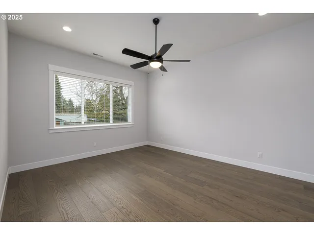 an empty room with wooden floor ceiling fan and windows