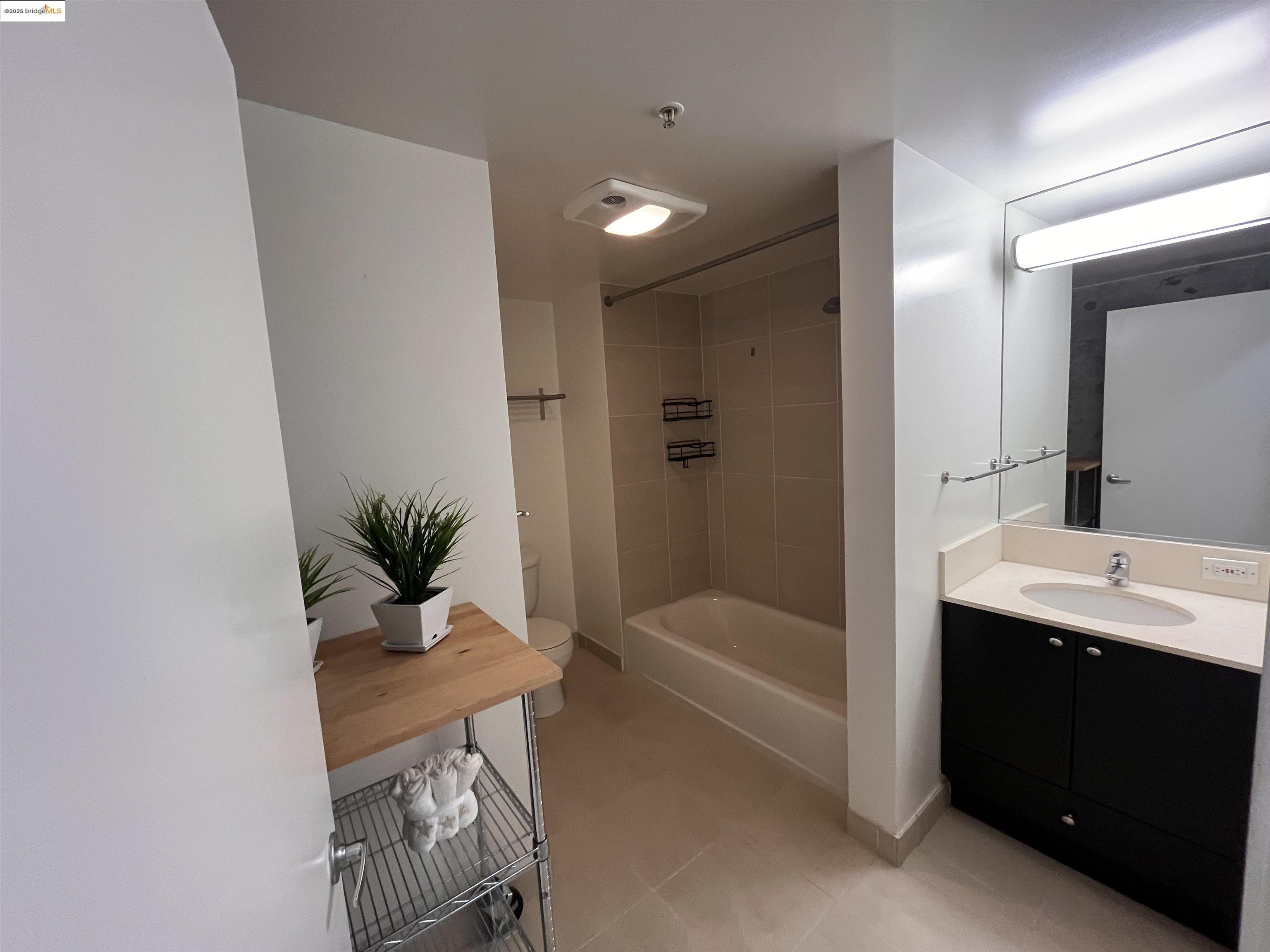 311 Oak Street, Unit 724 Oakland, CA 94607 - Photo 10 of 16 a bathroom with a granite countertop sink a mirror a bathtub and shower