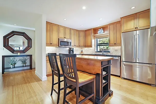 a kitchen with stainless steel appliances granite countertop a refrigerator a stove a sink a dining table and chairs with wooden floor