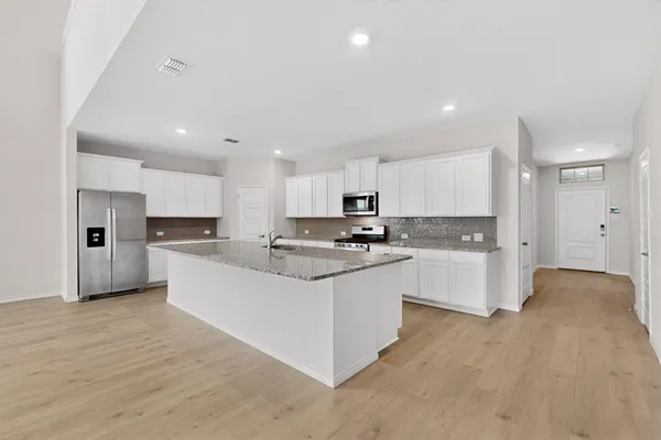 a large kitchen with stainless steel appliances kitchen island a sink dishwasher a refrigerator and white cabinets with wooden floor