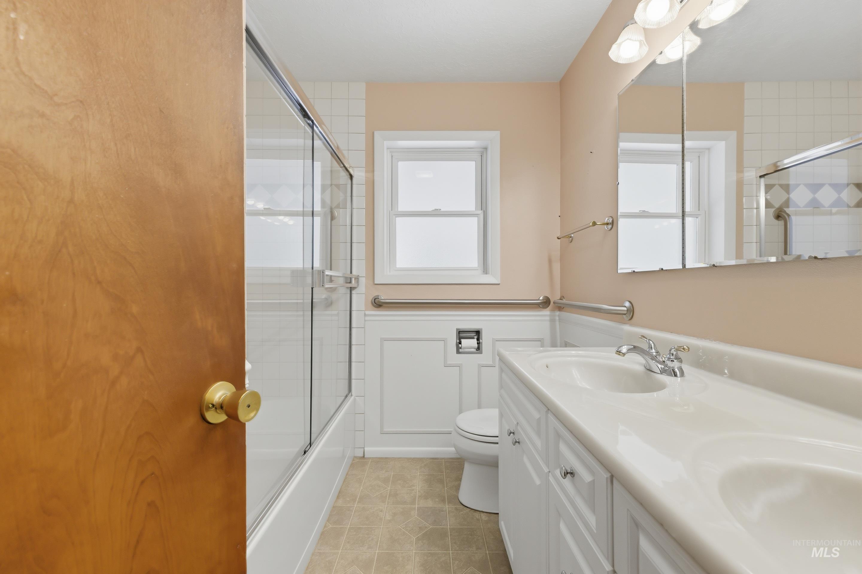 504 West Howe Street Boise, ID 83706 - Photo 27 of 47 Bathroom featuring a double vanity with integrated sinks, a tub/shower combination with glass enclosure, white wainscoting, and a window