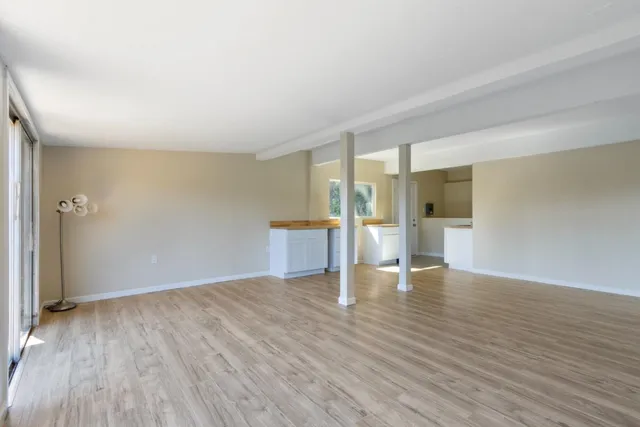 a view of a kitchen and an empty room with wooden floor and a kitchen