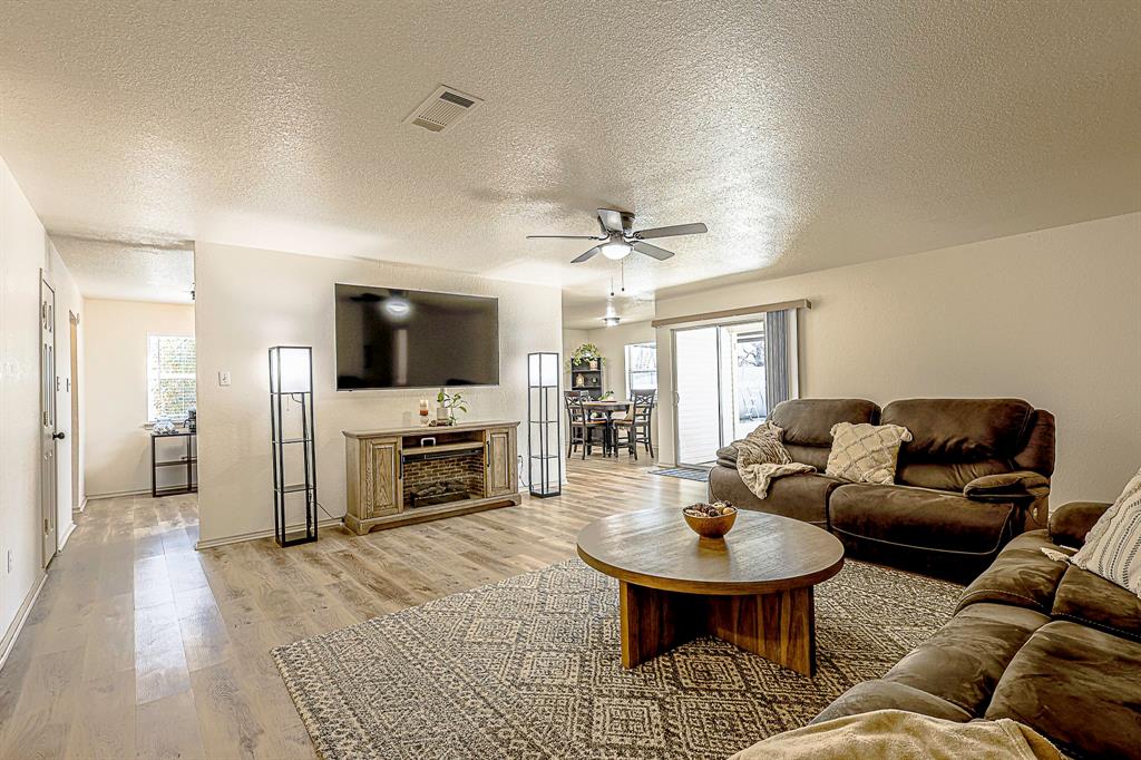 10812 Lilry Road Waco, TX 76708 - Photo 11 of 25 Living room featuring a textured ceiling, light wood-type flooring, healthy amount of natural light, and a ceiling fan