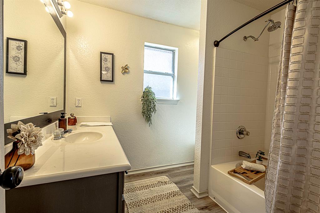 10812 Lilry Road Waco, TX 76708 - Photo 15 of 25 Bathroom featuring a textured wall, vanity, shower / bathtub combination with curtain, and dark wood-type flooring