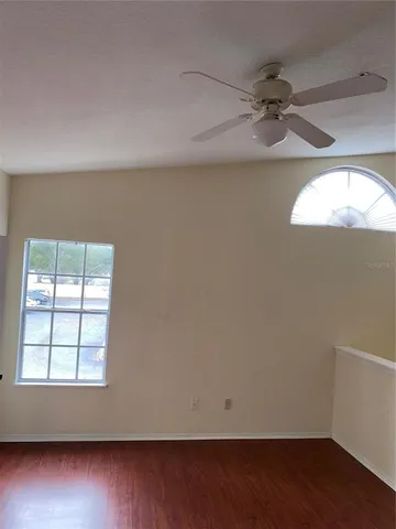 an empty room with wooden floor fan and windows