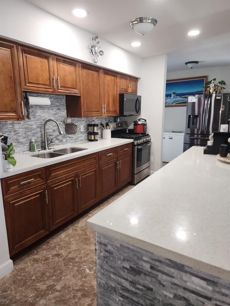 341 West 59th Street Hialeah, FL 33012 - Photo 32 of 44 a kitchen with stainless steel appliances granite countertop a sink dishwasher stove and refrigerator with wooden cabinets