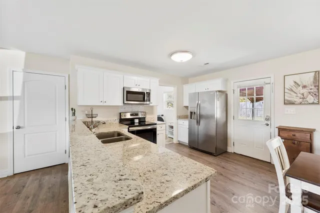 a kitchen with granite countertop a refrigerator a stove a sink a dining table and chairs