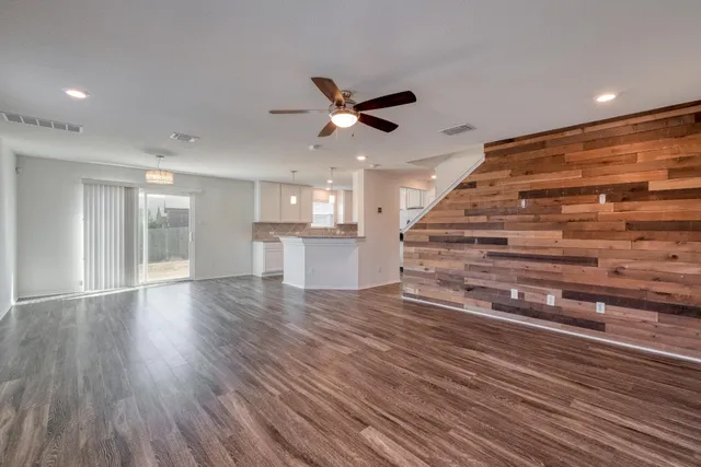 a view of an empty room with wooden floor and a ceiling fan