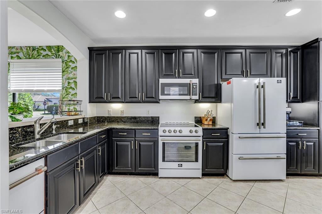 1307 Kendari Terrace Naples, FL 34113 - Photo 14 of 45 Kitchen with white appliances, dark stone counters, recessed lighting, light tile patterned floors, and dark cabinets