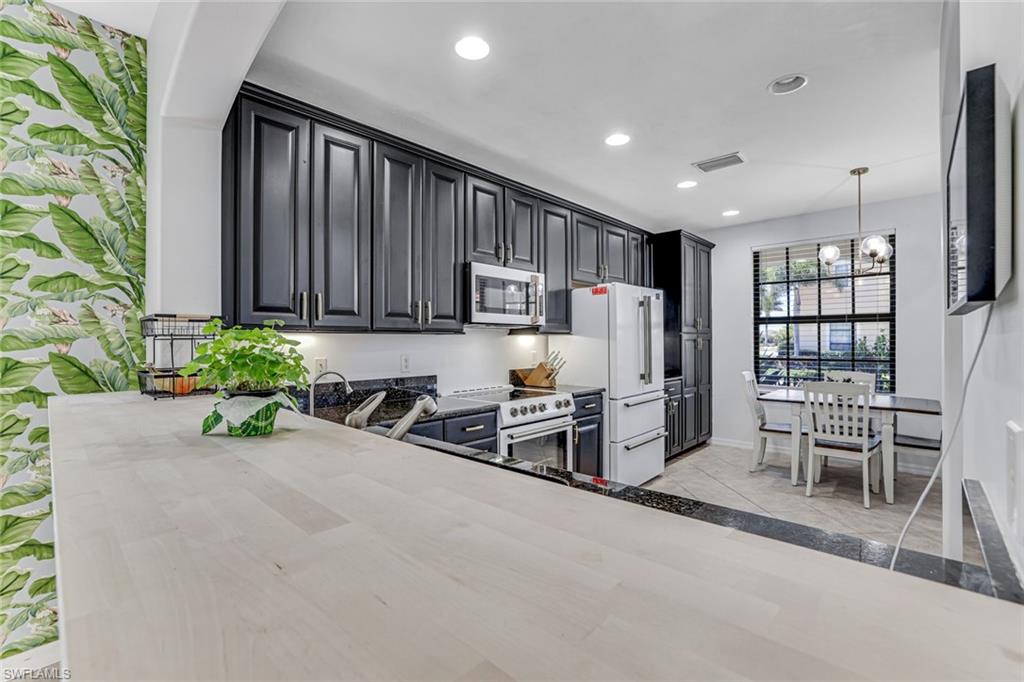 1307 Kendari Terrace Naples, FL 34113 - Photo 17 of 45 Kitchen with premium appliances, dark cabinetry, suspended lighting, a peninsula, and light stone countertops