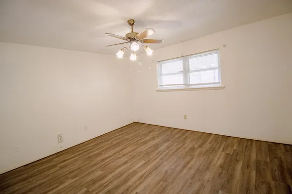 a view of an empty room with chandelier fan and wooden floor