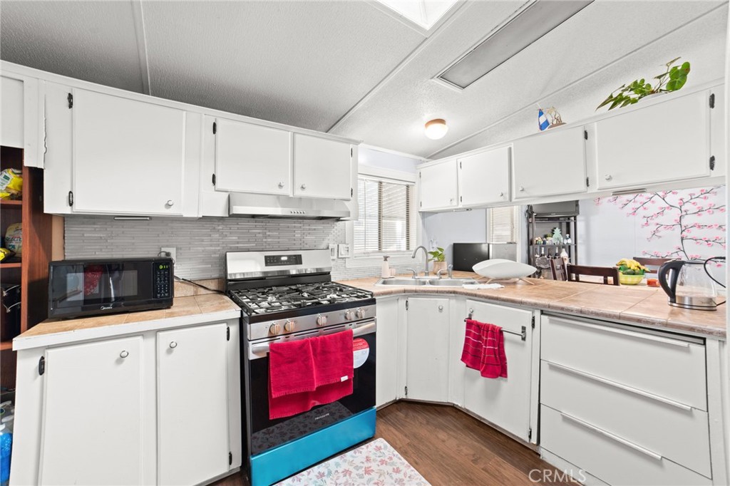 1155 South Riverside Avenue, Unit 22 Rialto, CA 92376 - Photo 13 of 34 a kitchen with a stove a sink dishwasher and white cabinets with wooden floor