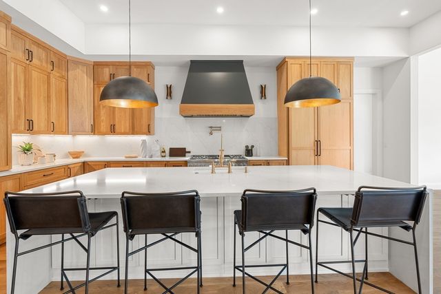 a large white kitchen with a large island oven a sink a stove and a dining table with garden view