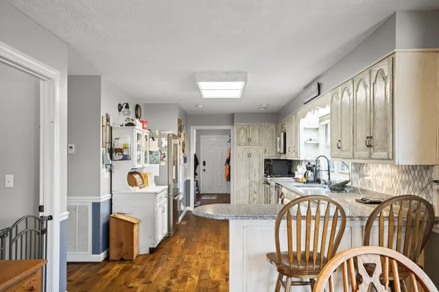 a kitchen with stainless steel appliances granite countertop a stove a sink dishwasher a refrigerator and white cabinets with wooden floor