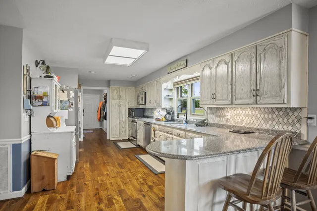 a kitchen with stainless steel appliances granite countertop a stove top oven a sink dishwasher a dining table and chairs with wooden floor