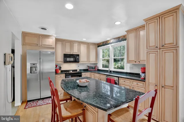 a kitchen with stainless steel appliances granite countertop a stove top oven a refrigerator a dining table and chairs with wooden floor