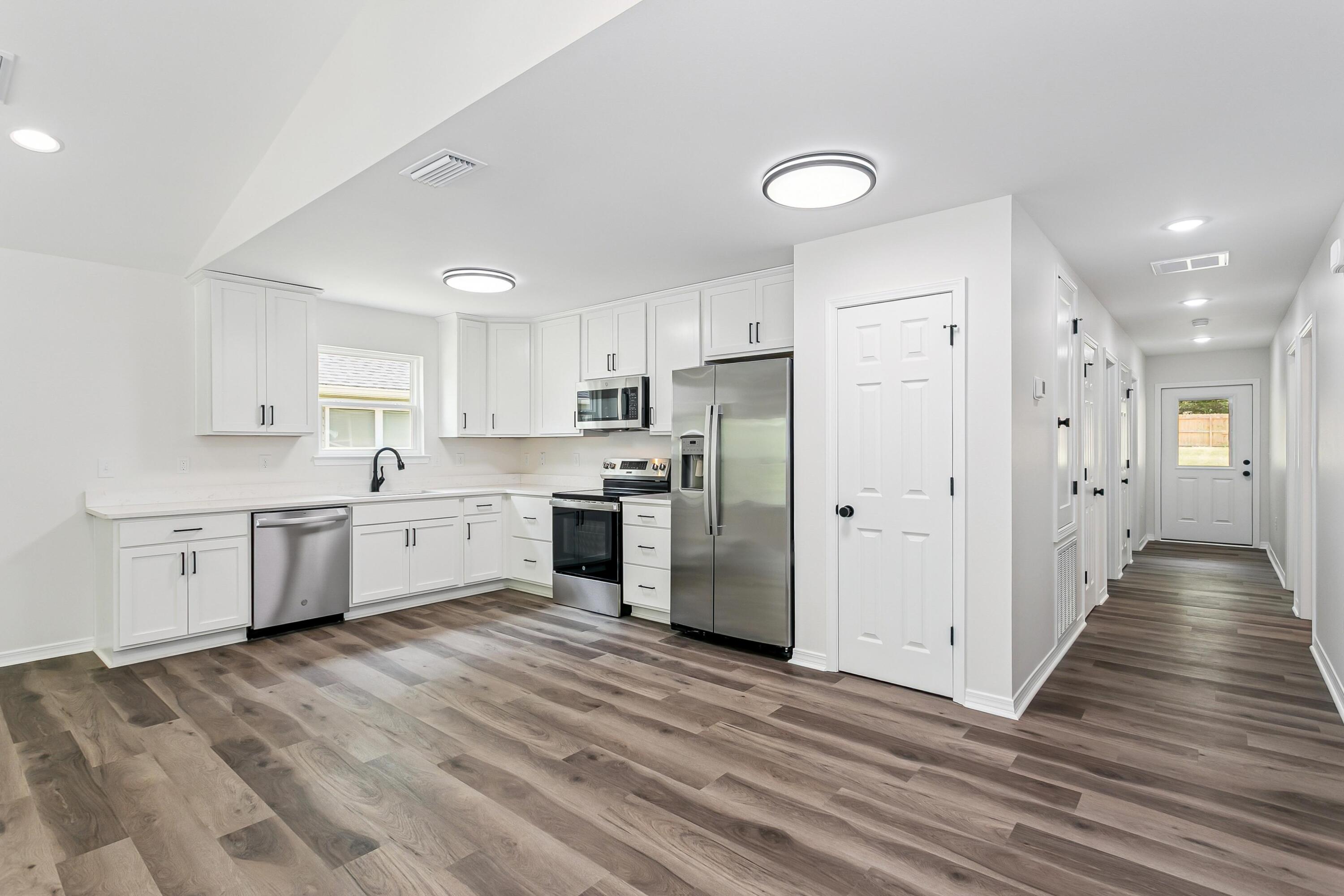 8084 3rd Street Laurel Hill, FL 32567 - Photo 15 of 34 a large kitchen with stainless steel appliances granite countertop a stove a sink dishwasher a refrigerator and white cabinets with wooden floor