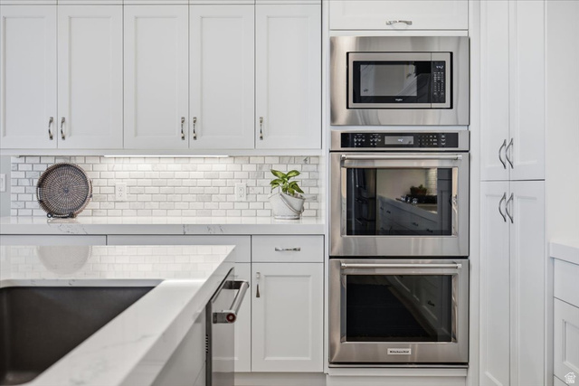 21 Pier Place Tooele, UT 84074 - Photo 24 of 112 Kitchen featuring white shaker cabinetry, stainless steel built-in appliances, undermount sink, white countertops, and a white subway tile backsplash with under-cabinet lighting