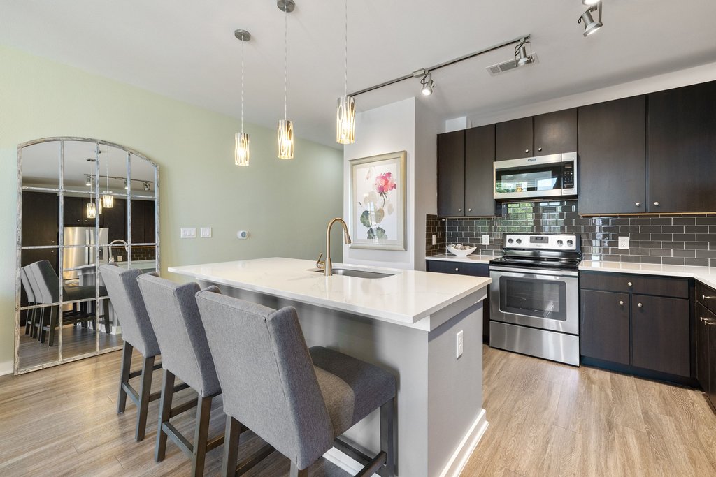 1900 Barton Springs Road, Unit 5009 Austin, TX 78704 - Photo 4 of 35 A contemporary kitchen features dark cabinetry, stainless steel appliances, and a central island with sleek white countertops.