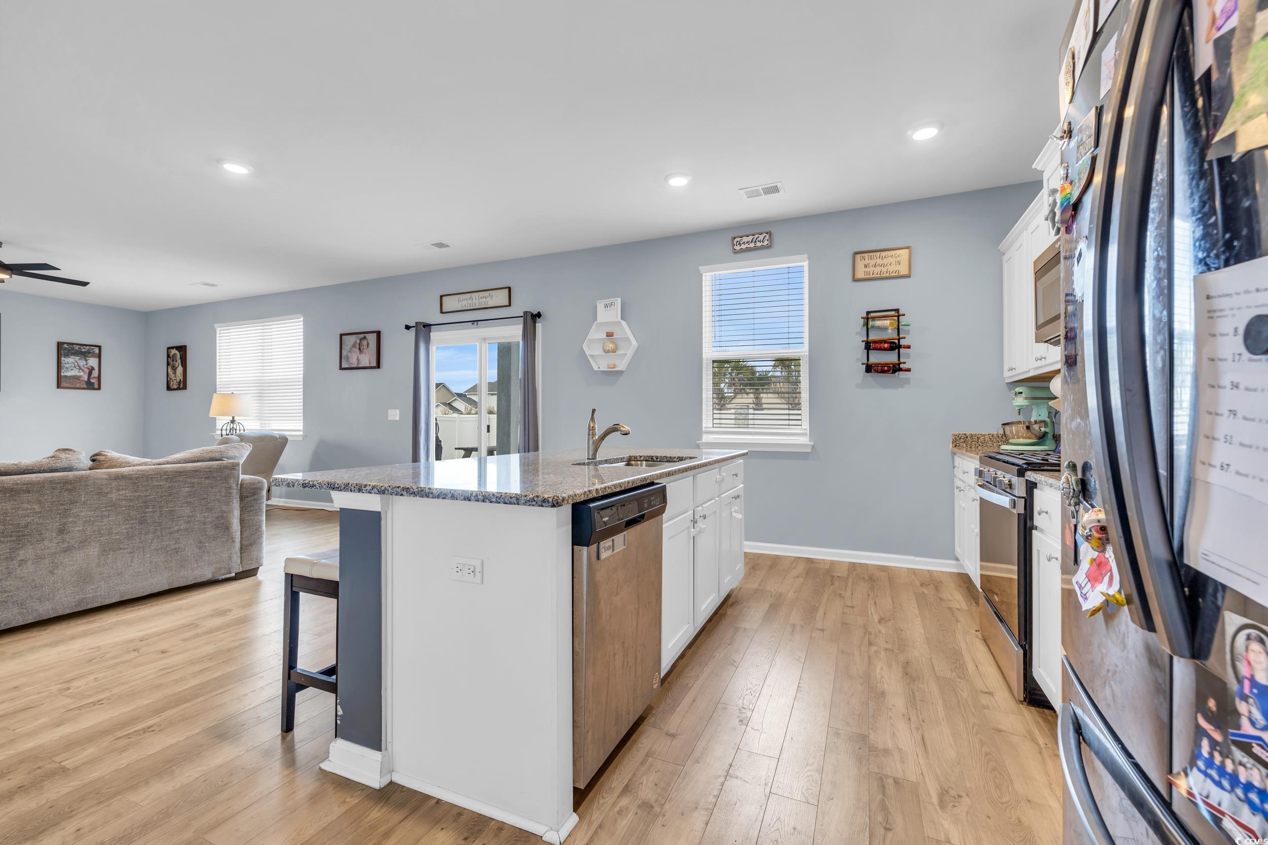 205 Black Pearl Way Myrtle Beach, SC 29588 - Photo 27 of 28 Kitchen featuring appliances with stainless steel finishes, a kitchen bar, open floor plan, white cabinets, and a kitchen island with sink