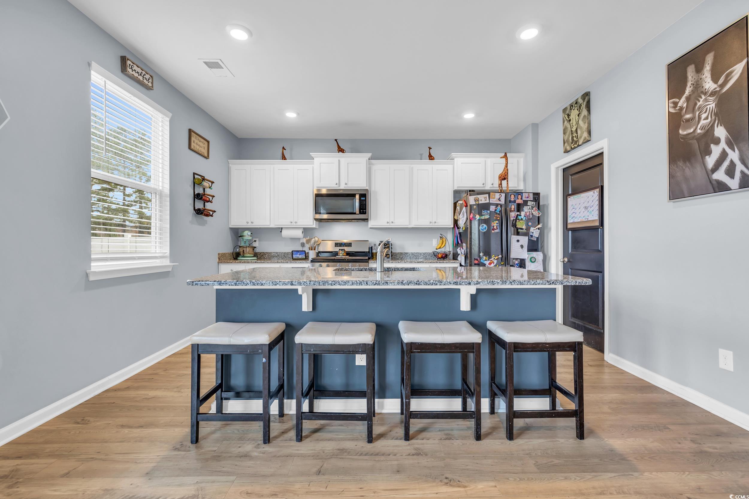 205 Black Pearl Way Myrtle Beach, SC 29588 - Photo 5 of 28 Kitchen featuring white cabinetry, appliances with stainless steel finishes, a breakfast bar, an island with sink, and light stone countertops