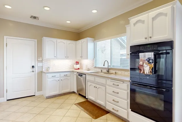 a large kitchen with stainless steel appliances a stove a sink a refrigerator and white cabinets with wooden floor