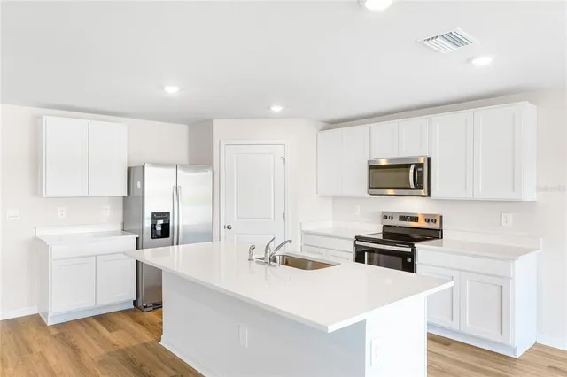 a kitchen with stainless steel appliances a sink a stove a microwave a center island and cabinets