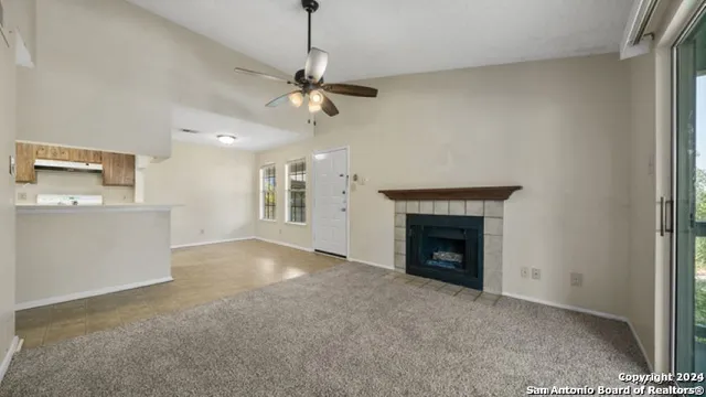 a view of a livingroom with a fireplace a ceiling fan and a kitchen view