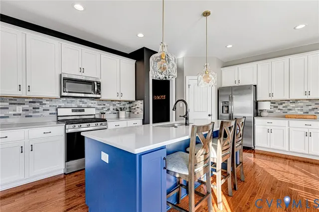 a kitchen with stainless steel appliances granite countertop a stove top oven a refrigerator a sink and a dining table with wooden floor