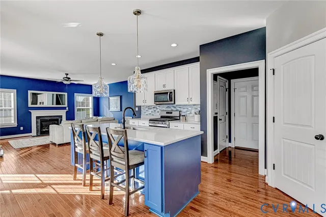 a kitchen with stainless steel appliances granite countertop a refrigerator a stove top oven a island a dining table and chairs with wooden floor