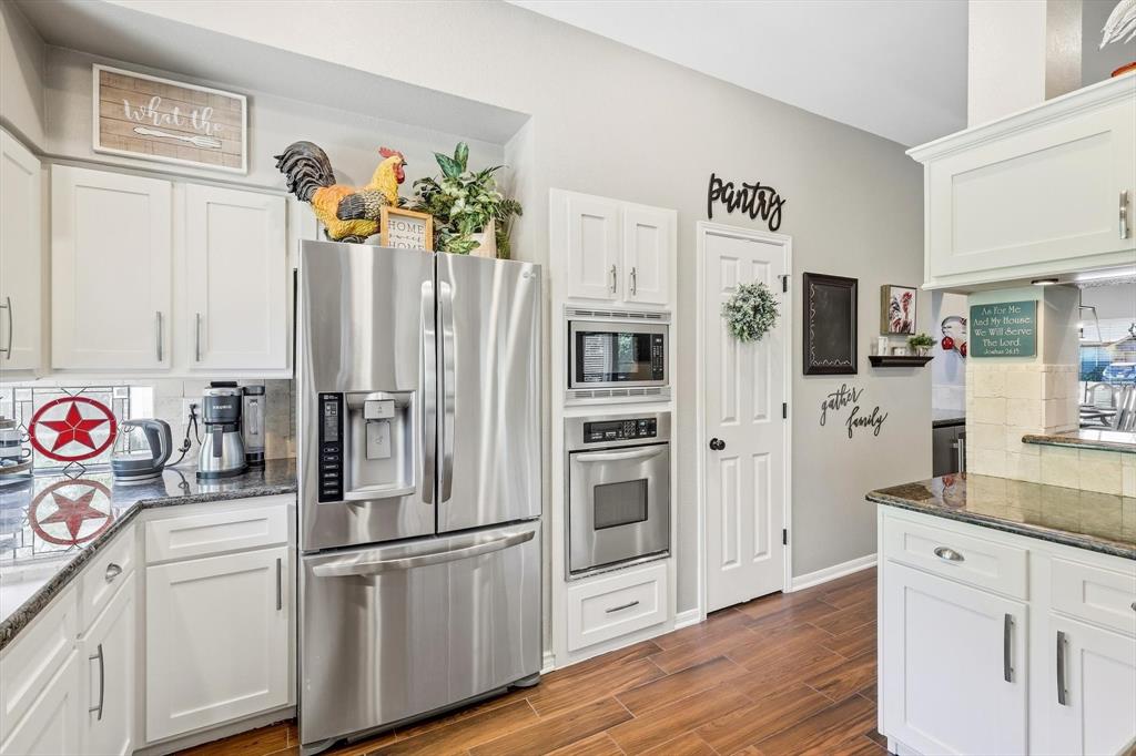 524 Post Oak Road Grapevine, TX 76051 - Photo 14 of 37 White cabinetry with sleek hardware, granite countertops, wood-finish flooring, stainless steel French door refrigerator, and built-in stainless steel microwave and oven
